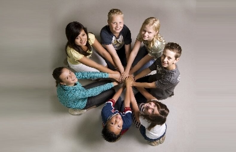 Kinderen zitten in een kringetje en leggen met uitgestrekte armen de handen op elkaar