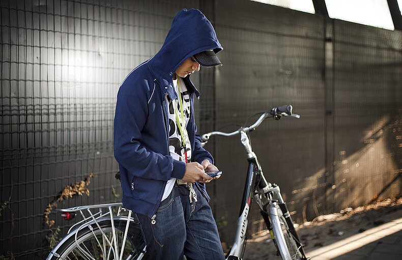 Jongen met mobiel hangt tegen fiets